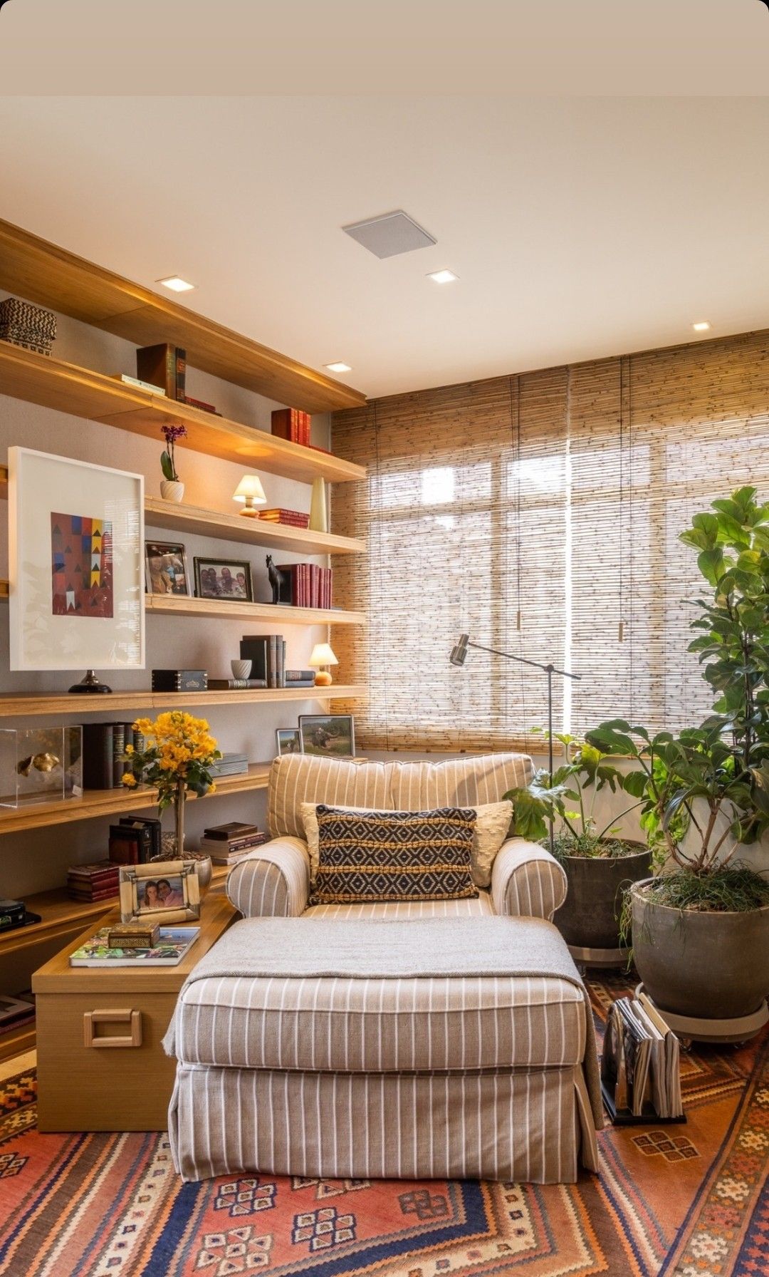 Sala de leitura com luz natural filtrada pela persiana e luminárias na estante